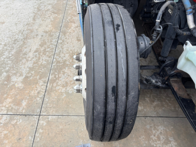 Kenworth T680 front wheel and tire assembly showing triple-ribbed dual-steel wheel with hub and brake components visible.