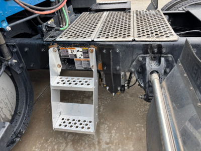 Kenworth T680 truck chassis showing aluminum perforated platform steps and surrounding mechanical components.