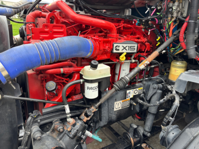KENWORTH T680 engine bay showing red V12? no, red  X15 engine with blue intake hose, white PACCAR fluid reservoir, various hoses and wiring.