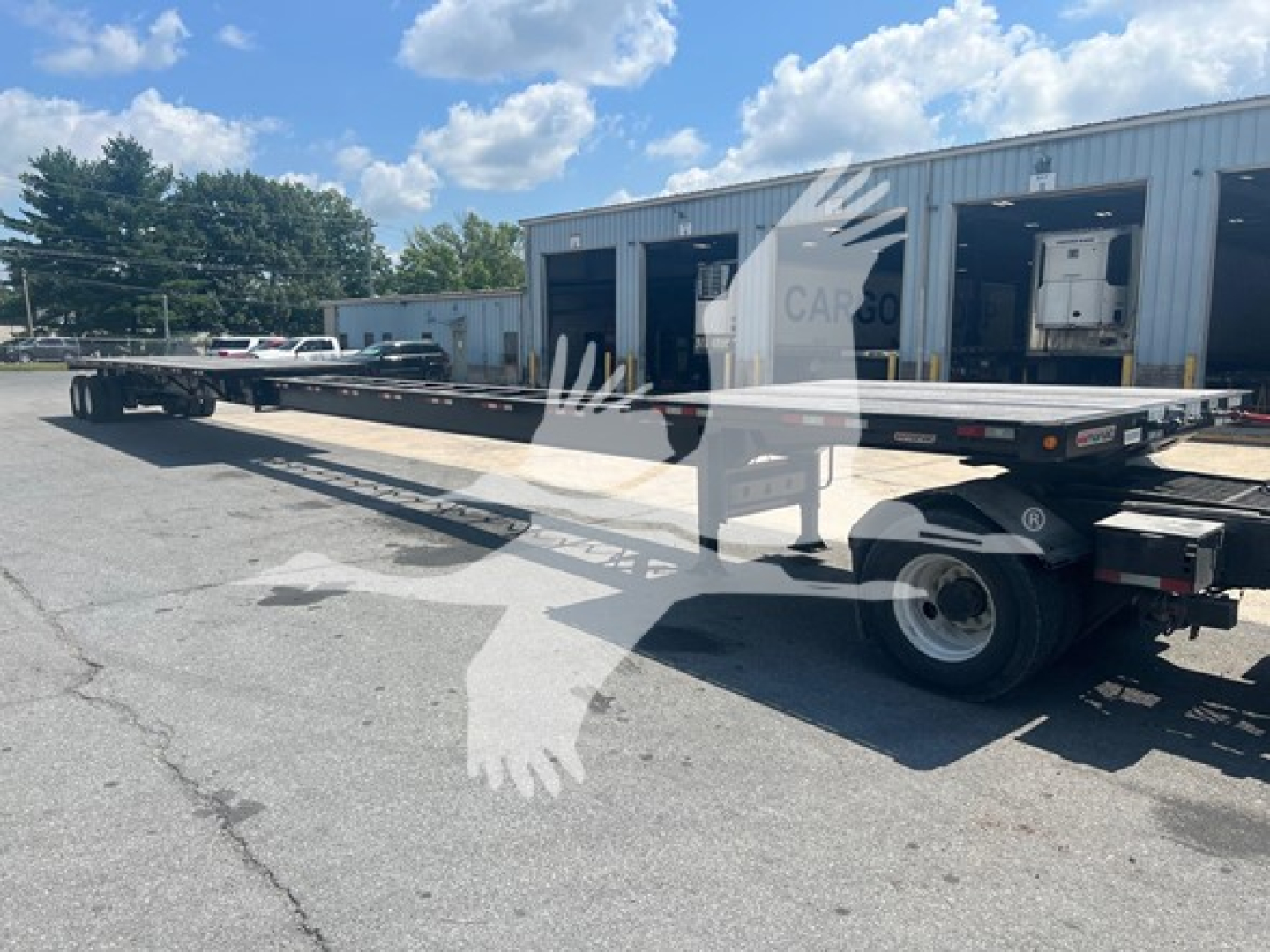 Flatbed trailer in service with extendable main deck, showing rear and side profile, MANAC branding faintly visible, hydraulic components and wheels.