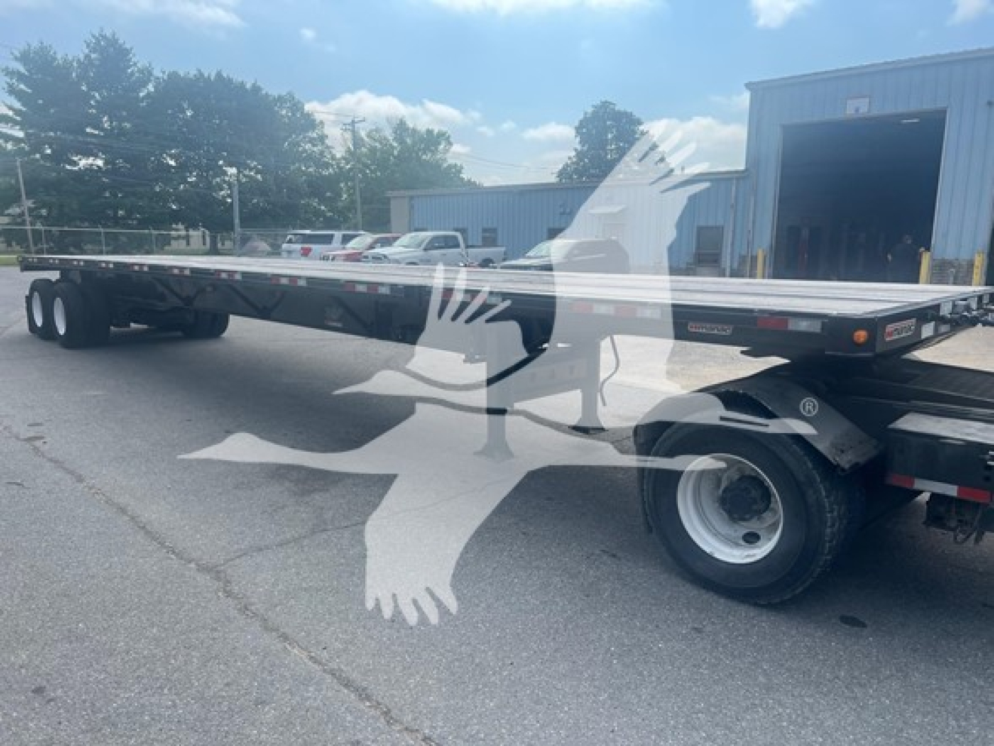 Manac flatbed trailer in an open lot, extendable spring steel deck with dual rear axles and white wheels; VIN and stock number not visible on the side.