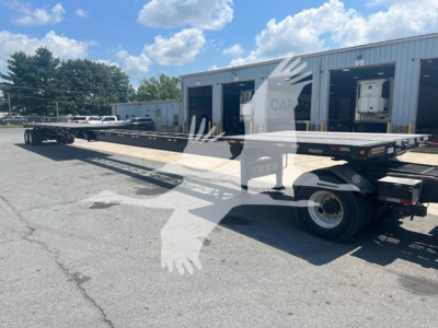 Flatbed trailer in service with extendable main deck, showing rear and side profile, MANAC branding faintly visible, hydraulic components and wheels.