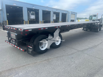 Manac spring extendable flatbed trailer with dual rear axles and extendable deck, viewed from side at a truck yard.
