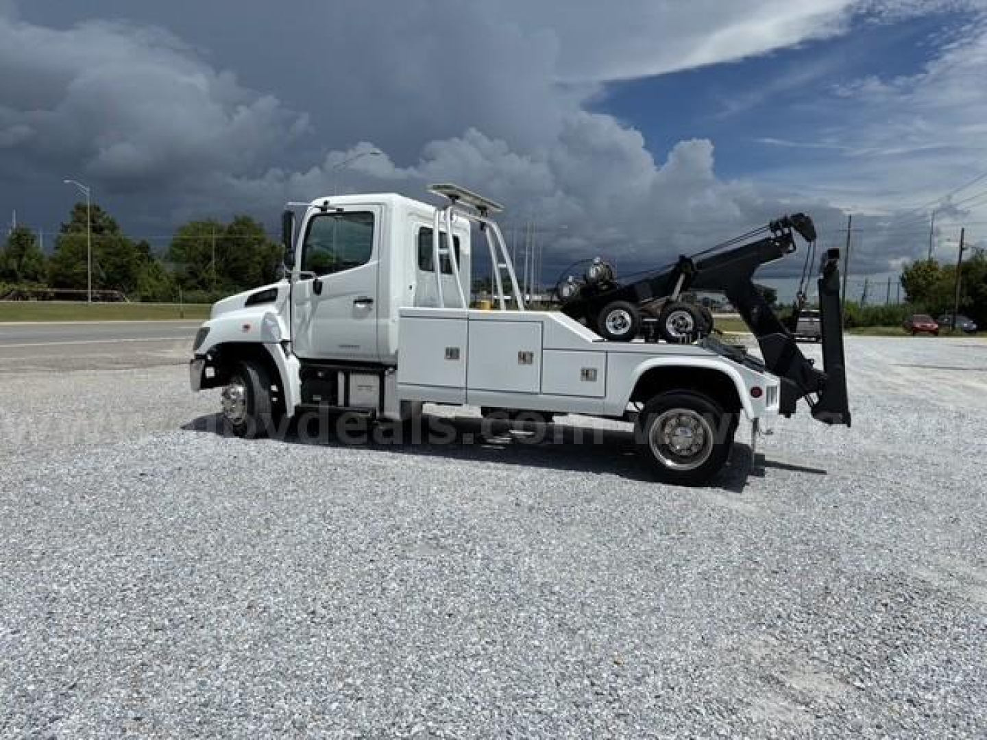 Tow truck with Hino cab and integrated wench/boom, side view showing rear wheel and hook lift on white body.