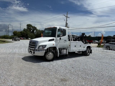 2018 Hino conventional cab tow truck front-left view showing flatbed and dual fuel doors with VIN and stock barcode area.