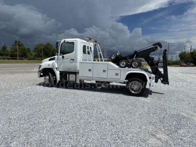 Tow truck with Hino cab and integrated wench/boom, side view showing rear wheel and hook lift on white body.