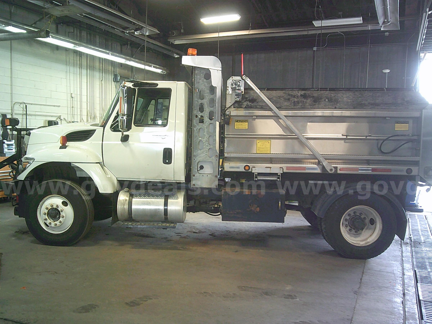 Truck side view showing a white 2011 International WorkStar 7400 dump truck with a metal dump bed inside a garage.