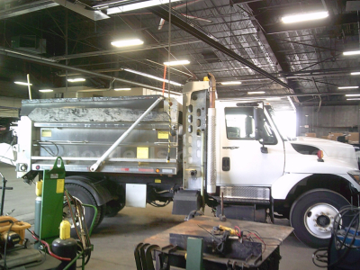 International WorkStar 7400 dump truck inside shop with side-view showing cab and dump bed, visible decals and equipment around.