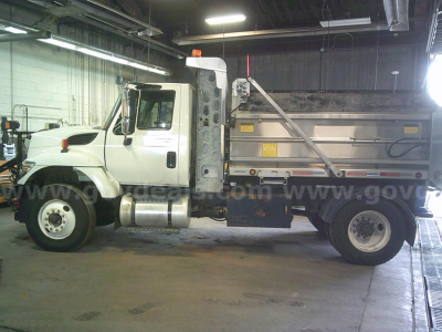 Truck side view showing a white 2011 International WorkStar 7400 dump truck with a metal dump bed inside a garage.