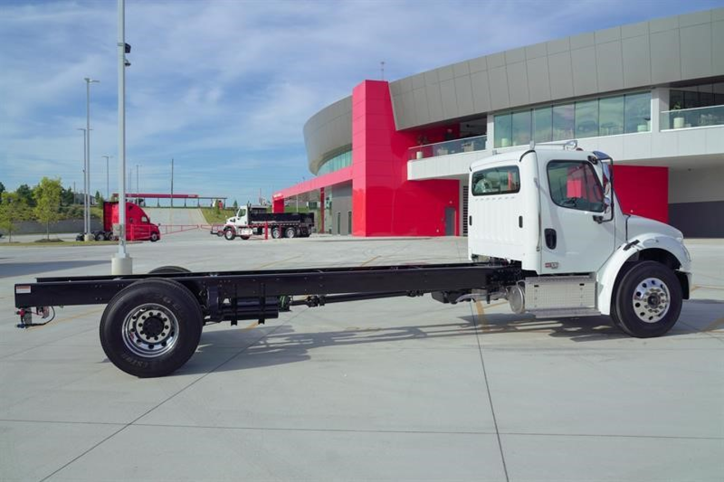Cab and chassis truck with long flatbed showing Freightliner M2 106 Plus styling in showroom lot.