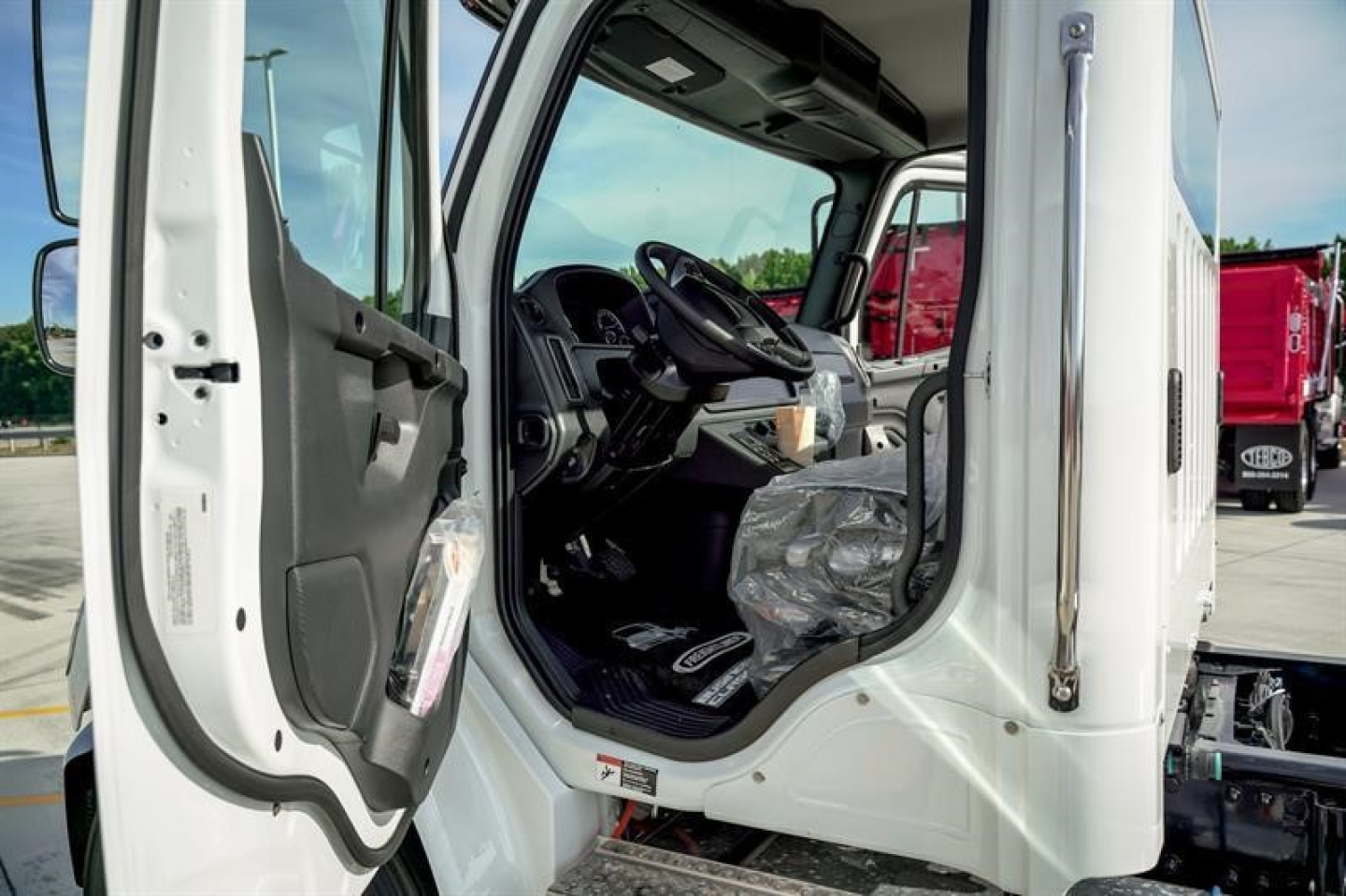 Freightliner M2 106 Plus cab interior showing steering wheel and driver seat; open door with dashboard and entry step visible.