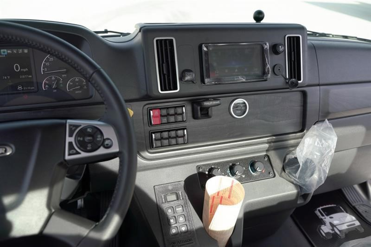 Cab interior of a Freightliner M2 106 Plus showing steering wheel, dashboard, touchscreen display, air vents, and control panel with buttons.