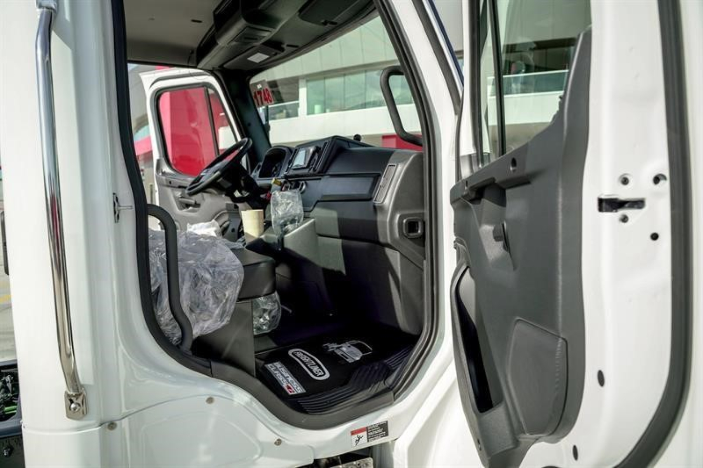 Truck cab interior view of a 2027 Freightliner M2 106 Plus showing driver seat and dashboard from open door.