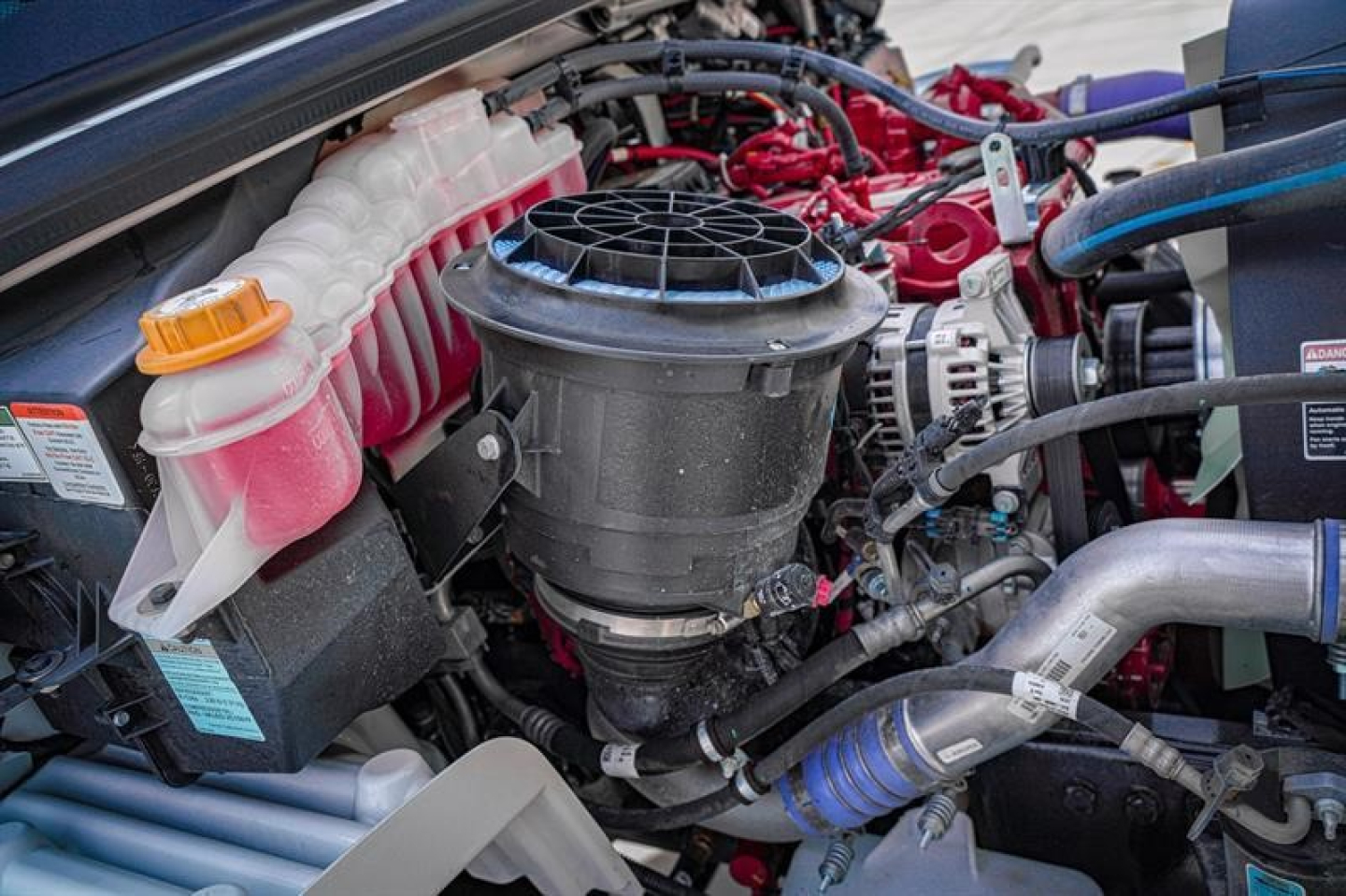 Engine bay of a Freightliner M2 106 Plus showing air intake, coolant reservoir with pink fluid, and wiring harnesses.