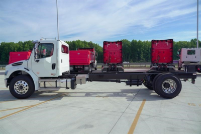 Freightliner M2 106 Plus cab and chassis with white cab and long chassis frame in an empty lot.