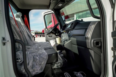 Cab interior of a new 2027 Freightliner M2 106 Plus showing dashboard, steering wheel, and plastic-covered driver and passenger seats.