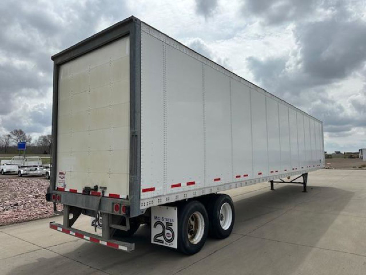 Trailer side and rear showing a 2016 Wabash van trailer with boxy aluminum sides, dual rear axles, and a license-style plate on rear with safety stickers. Visible text includes stock and VIN on the back area.