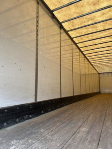 Van trailer interior showing wooden floor and side walls with vertical tracks and metal supports.