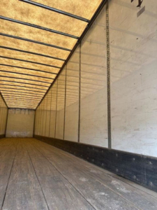 Inside of a Wabash van trailer showing wooden floor and white interior walls with vertical ribs and a translucent roof.