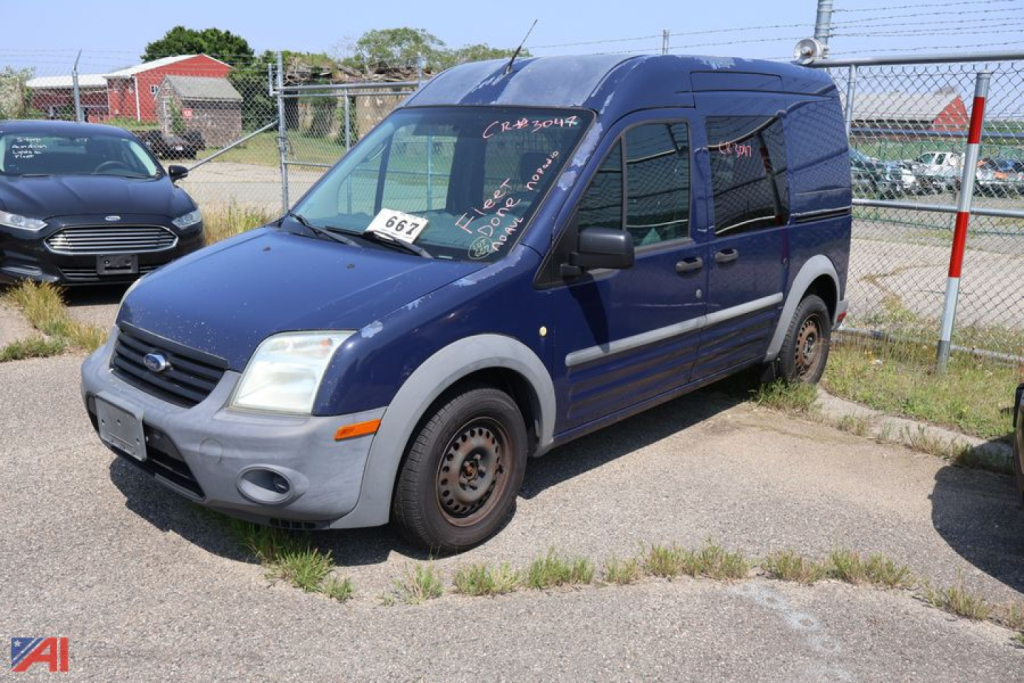 Ford Transit Connect cargo van with blue body and gray front bumper, side quarter panels, and missing front wheel; VIN/stock numbers on windshield.