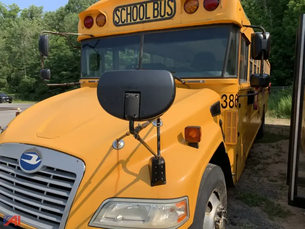 School bus front-left view showing yellow body, chestnut blue logo on grille, large black stop mirrors, and 'SCHOOL BUS' sign at top. Side number 38 visible and front corner marker lights.