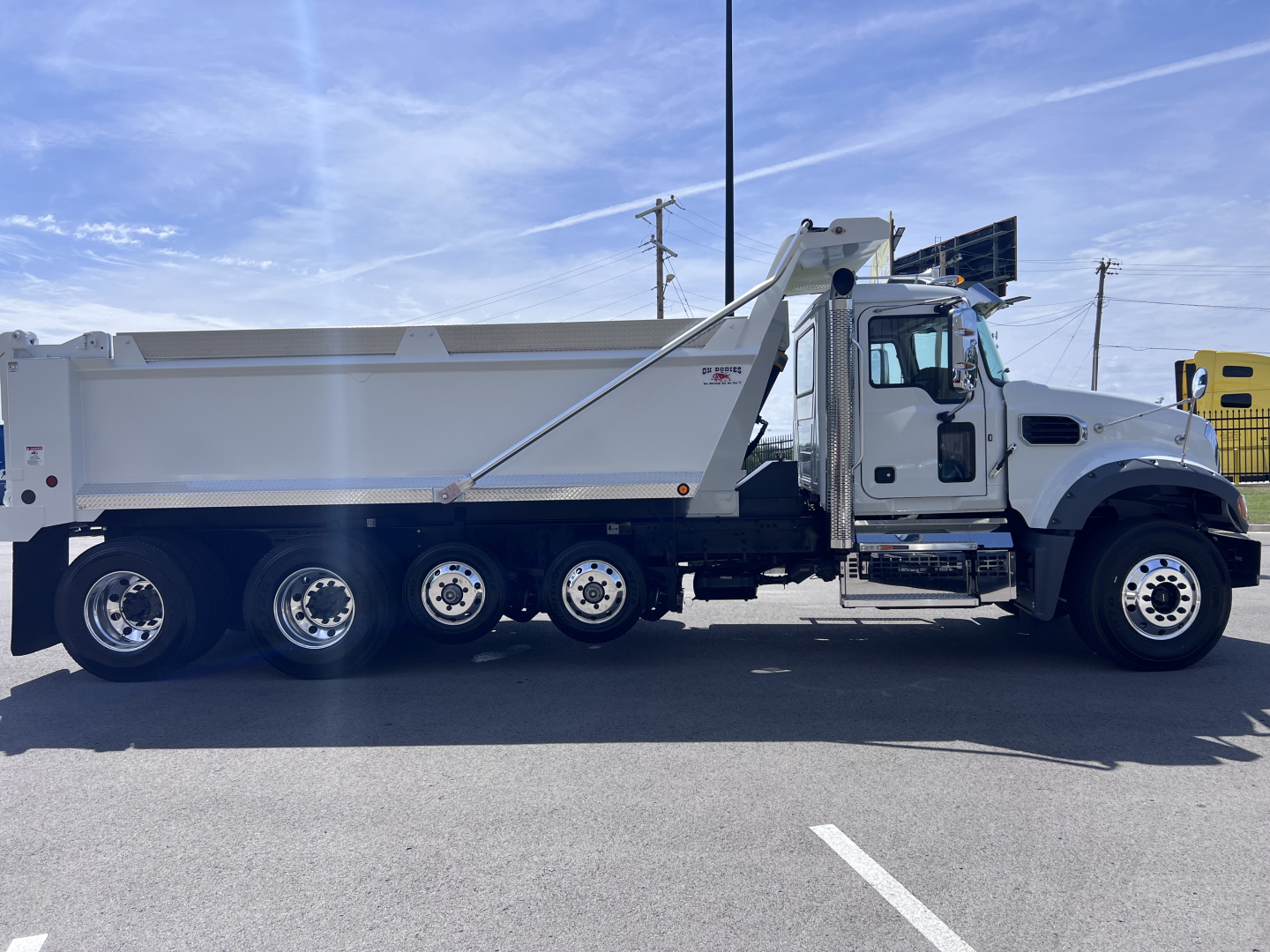 Dump truck side view showing 6x4 Mack GR64F chassis with white cab and large dump bed, VIN 1M2GR4GC3VM057395 on listing; stock 72243.