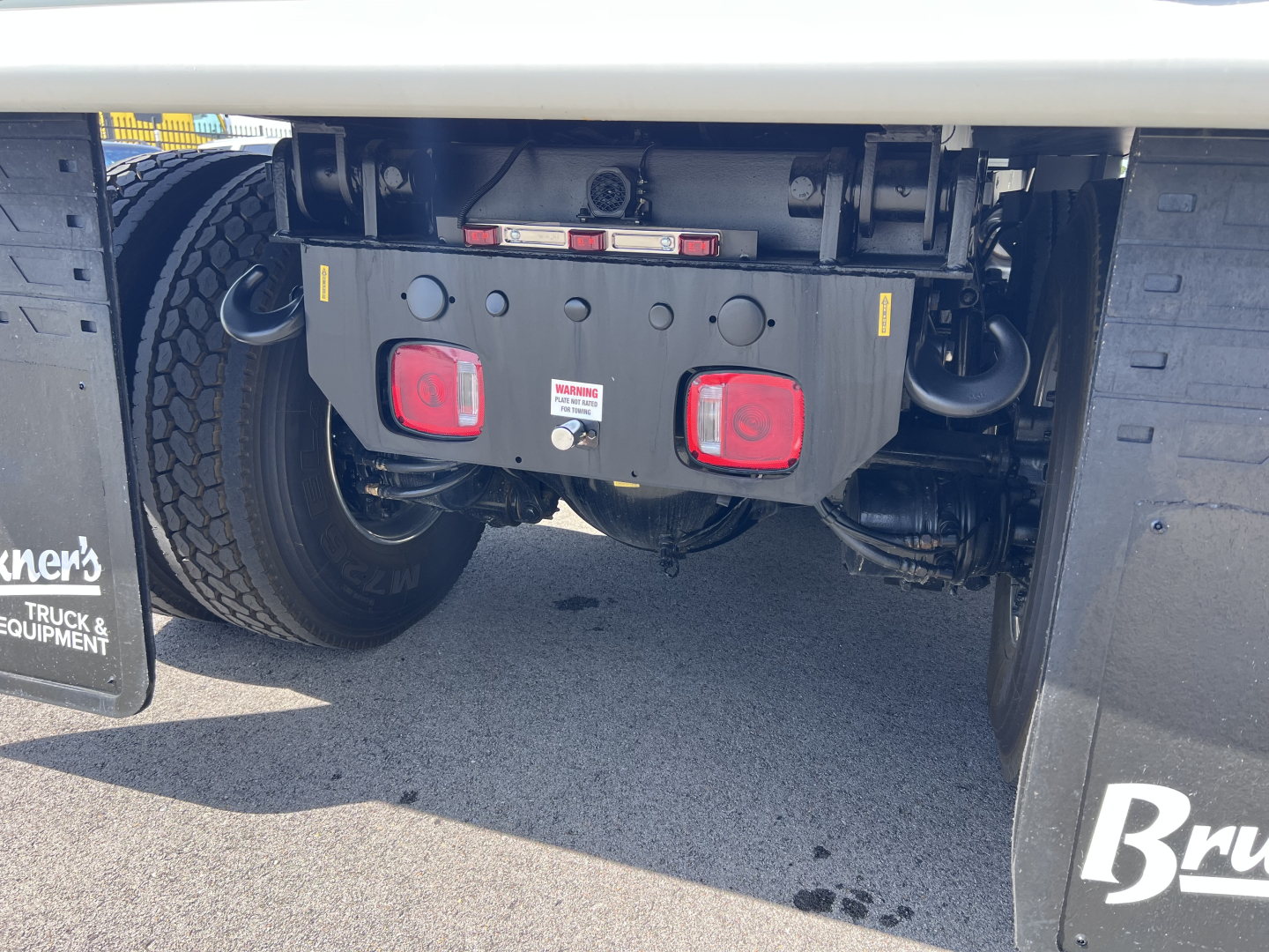 Mack GR64F rear underride bumper and suspension components showing tow hooks and warning labels.
