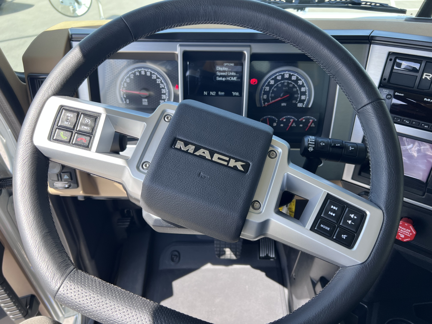 Steering wheel and instrument cluster of a Mack GR64F dump truck interior showing Mack emblem on center pad and steering wheel controls.