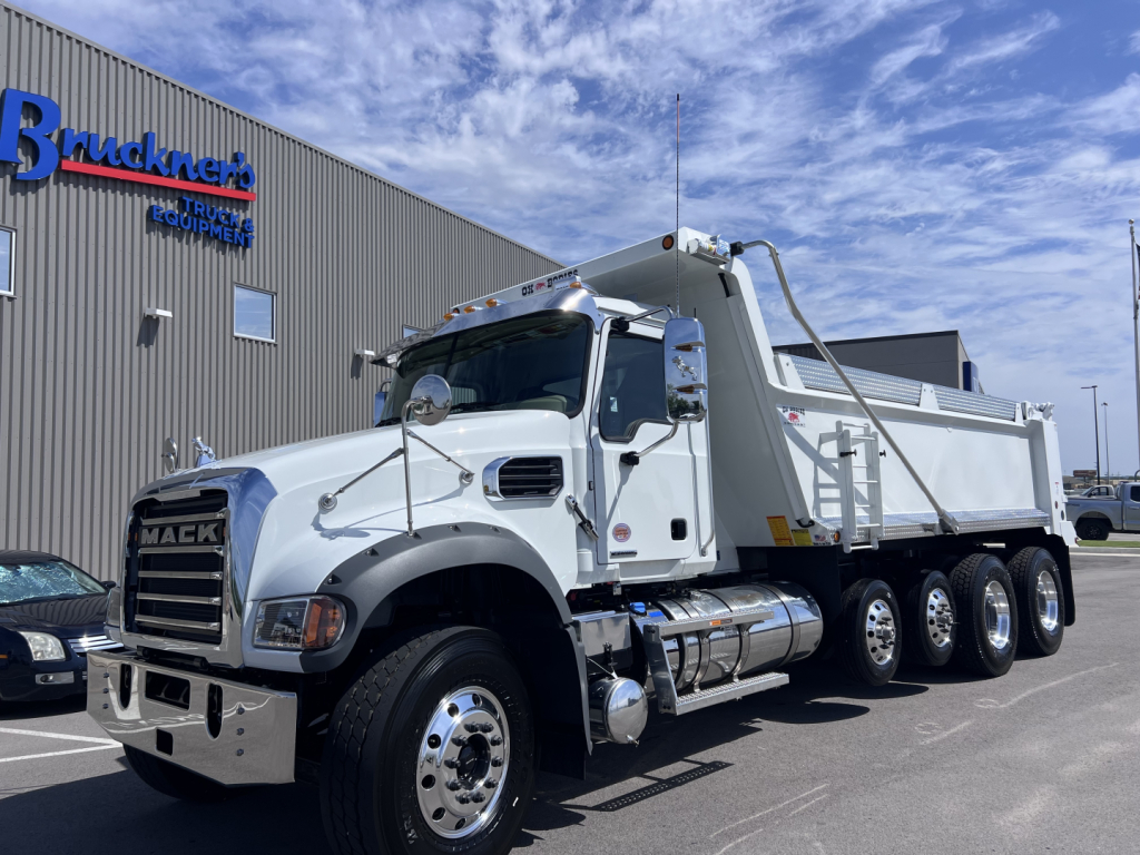 Mack GR64F dump truck in side view showing cab front grill and chrome bumper with triple rear axles and dumped bed.