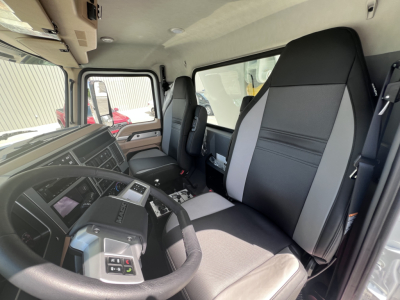 Truck cab interior of a 2027 Mack GR64F showing steering wheel, dashboard, driver seat, passenger seat, and center console.