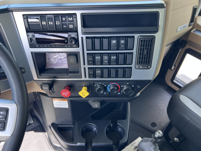 Dashboard of a 2027 Mack GR64F showing steering column area, gear selector, climate controls, auxiliary switches, and cup holders.
