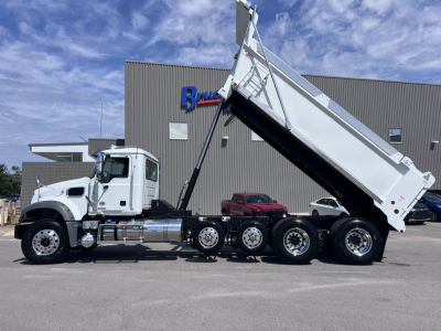 Truck chassis with dump body raised, side view of a Mack GR64F dump truck in front of a dealership.