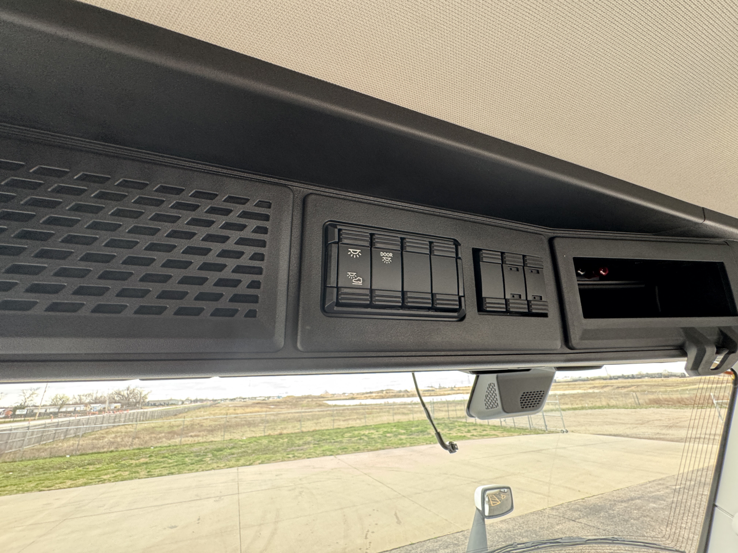 Instrument panel area of a 2026 Mack PR64T truck interior showing control switches and overhead console with a small display window.