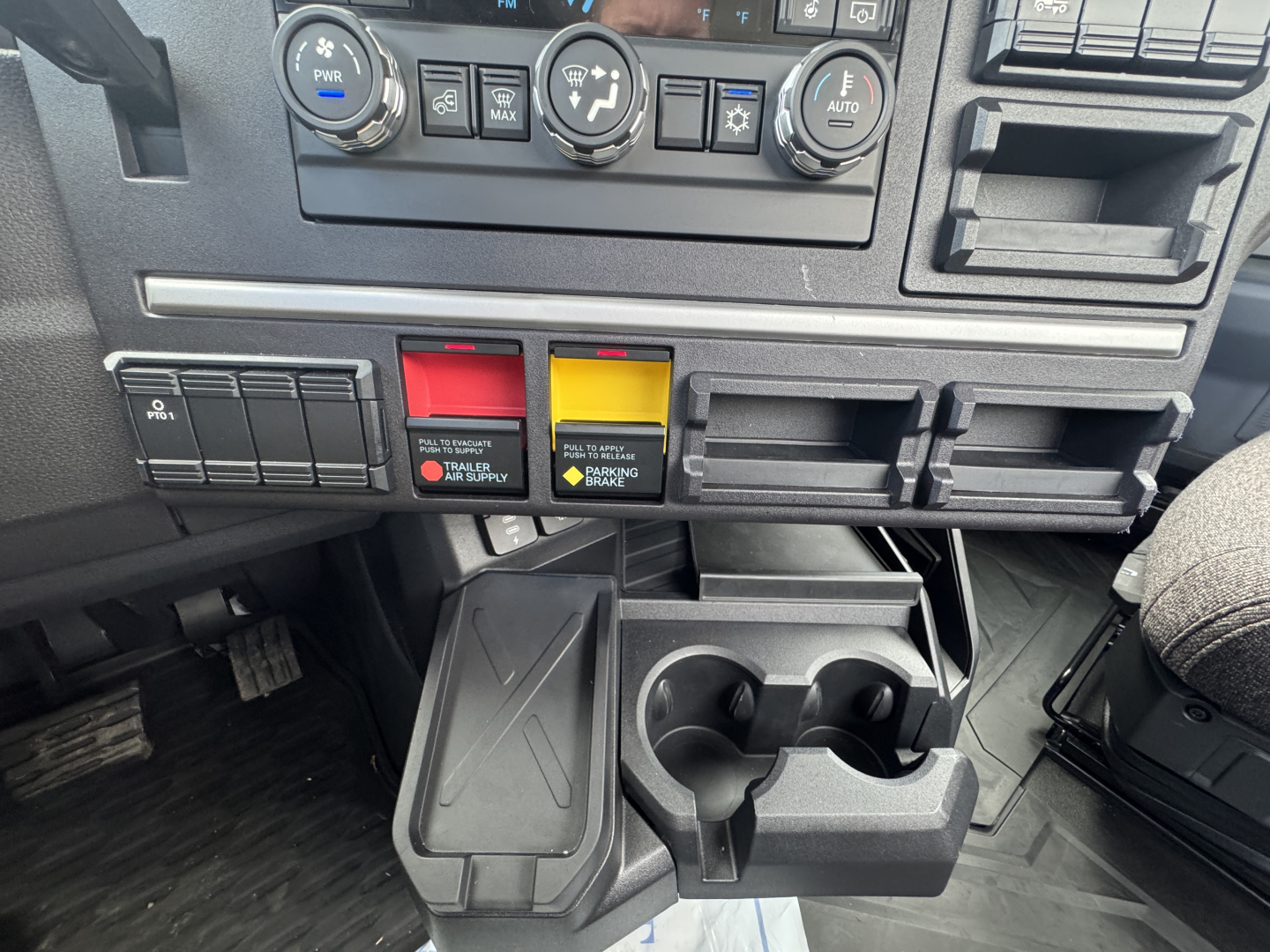 Dashboard area of a 2026 Mack PR64T showing climate controls, switch panels, and center cup/phone holder assembly.