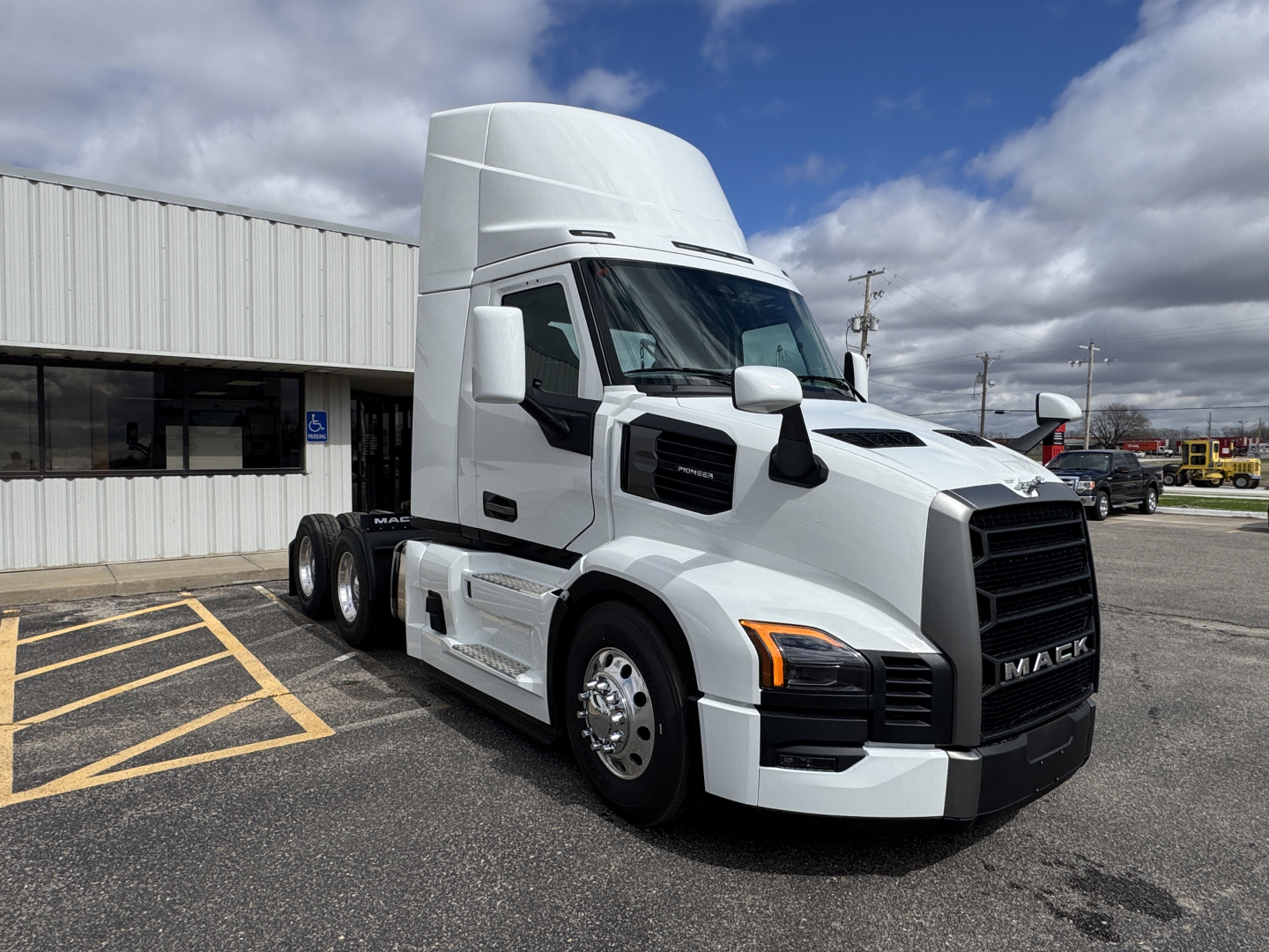 Truck cab: 2026 Mack PR64T conventional daycab with white paint, black grille, large sleeper/high roof, dual rear axles, chrome mirrors, in-service look.