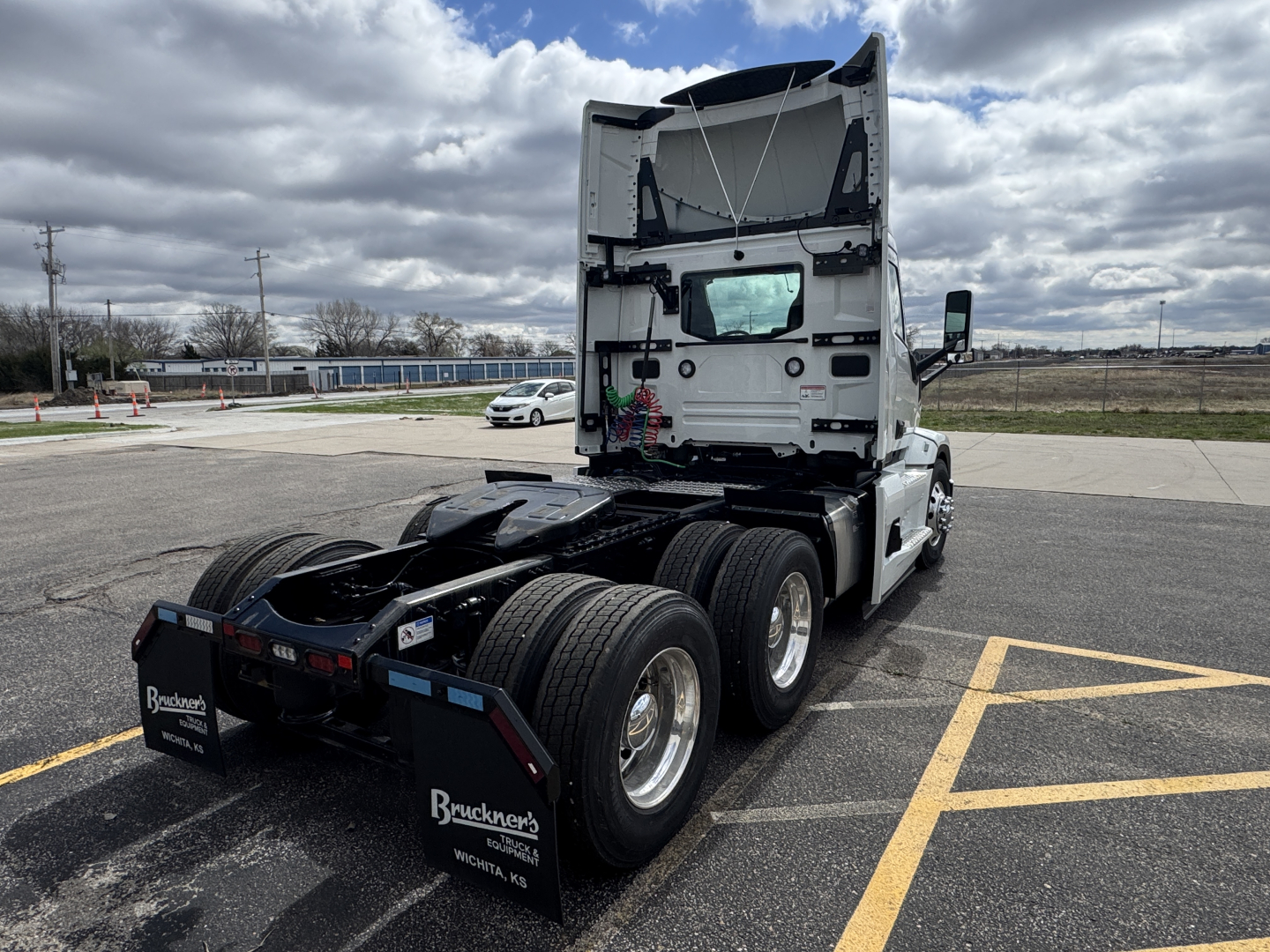 Truck cab rear and chassis of a 2026 Mack PR64T tractor seen from rear left angle in a parking lot; no visible text on side; rear shows tires and braking components.