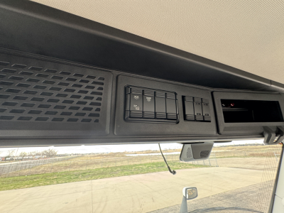 Instrument panel area of a 2026 Mack PR64T truck interior showing control switches and overhead console with a small display window.