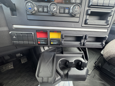Dashboard area of a 2026 Mack PR64T showing climate controls, switch panels, and center cup/phone holder assembly.