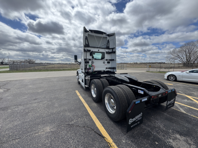 Rear view of a Mack PR64T truck tractor with mudflaps and dual rear axles in a parking lot. Visible text includes branding on mudflaps and components at the rear.