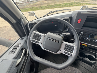 Steering wheel and dashboard of a Mack PR64T truck cab with multiple control buttons on the steering wheel and instrument cluster visible.