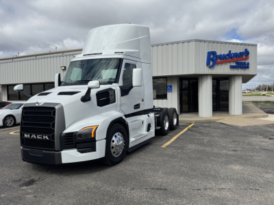 Mack PR64T tractor (cab and front) in white, 3-axle configuration, in front of a dealership building with Mack logo visible.