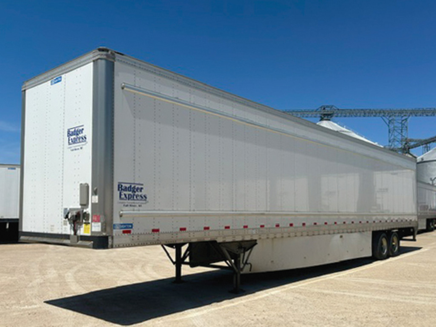 Stoughton trailer in outdoor lot showing aluminum side, tandem axle, and rear ramp door with Badger Express and blue decal stickers.
