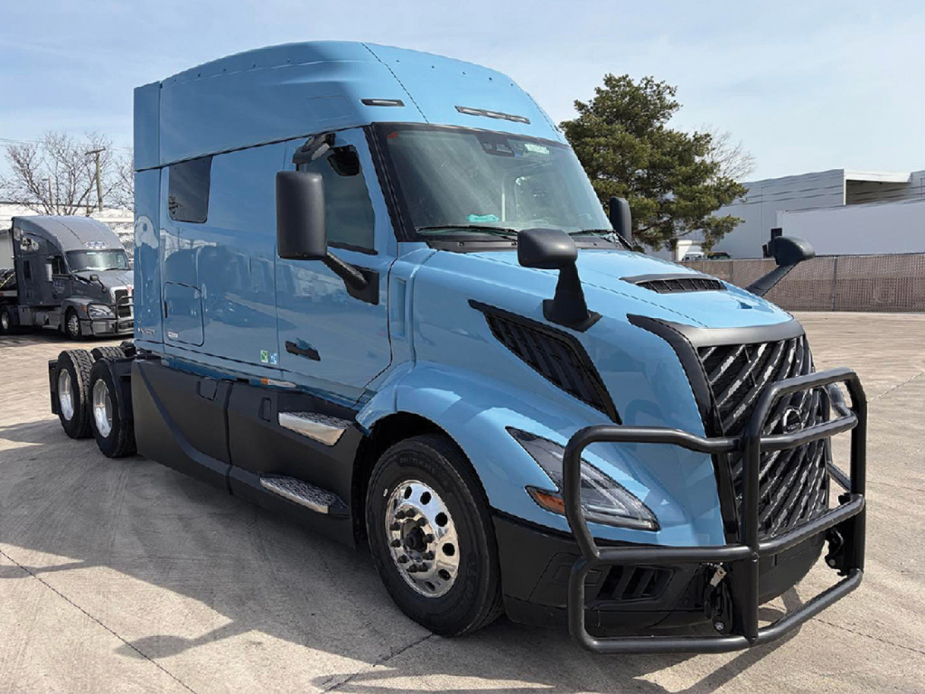 Volvo VNL 840 tractor trailer in blue with grille guard and side mirrors, three-axle configuration, long sleeper cab, parked in lot.