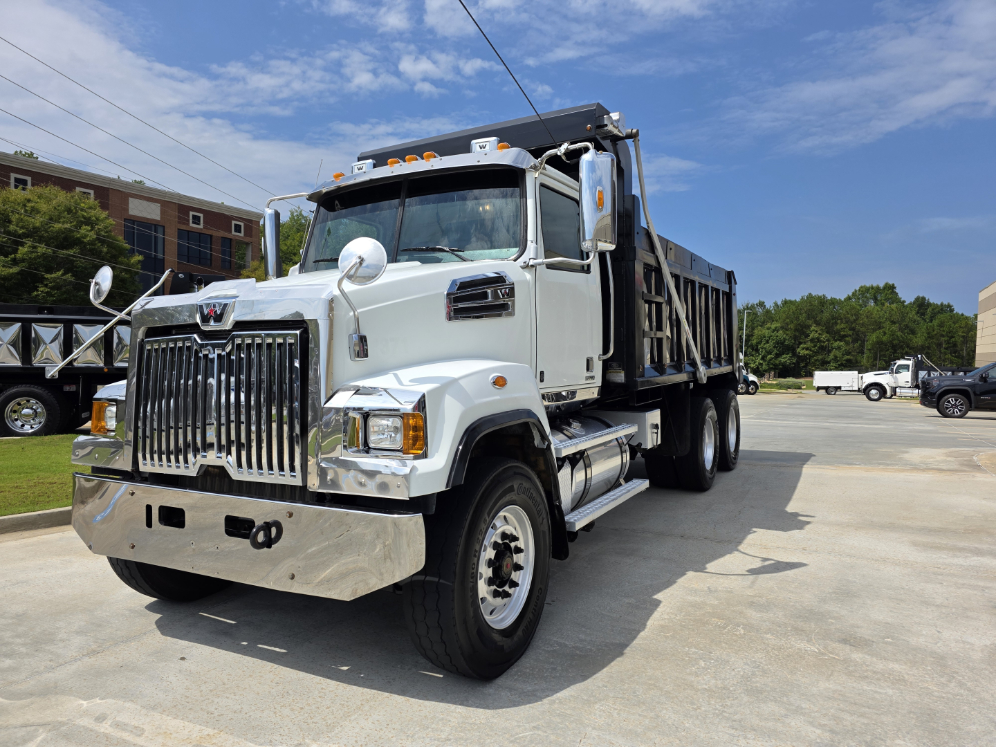 Truck in a dump body configuration with chrome grille, dual exhaust, and reflective mirrors. Front view of a 2022 Western Star 4700SF dump truck showing cab, headlights, and dump bed.