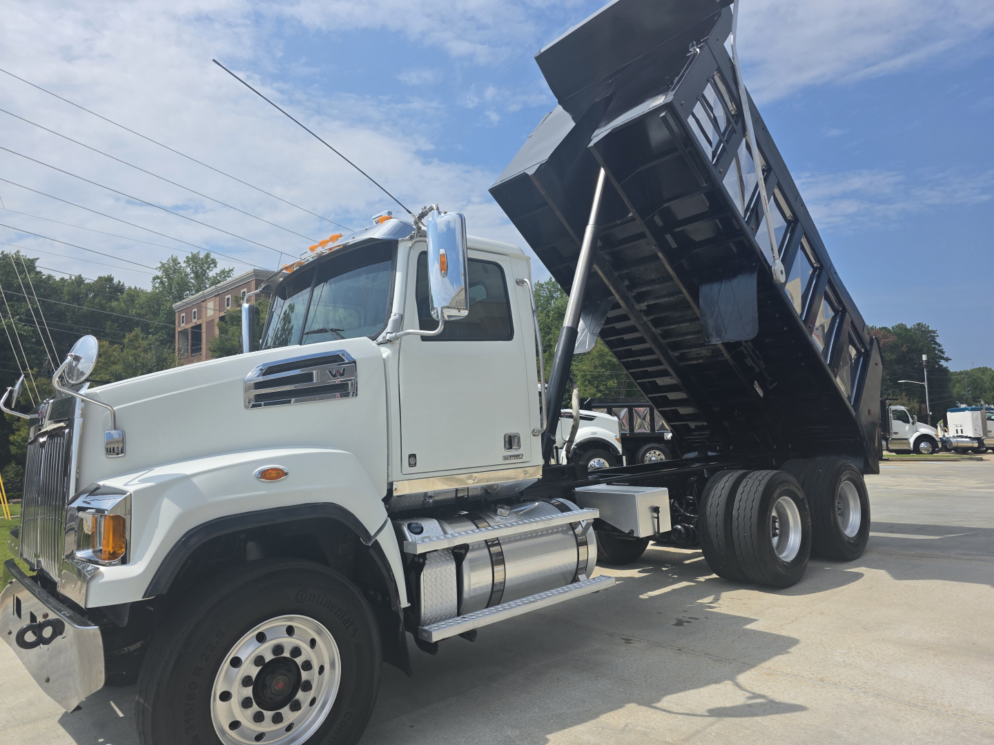 Western Star dump truck with raised dump bed in a dealership lot showing side view and cab.