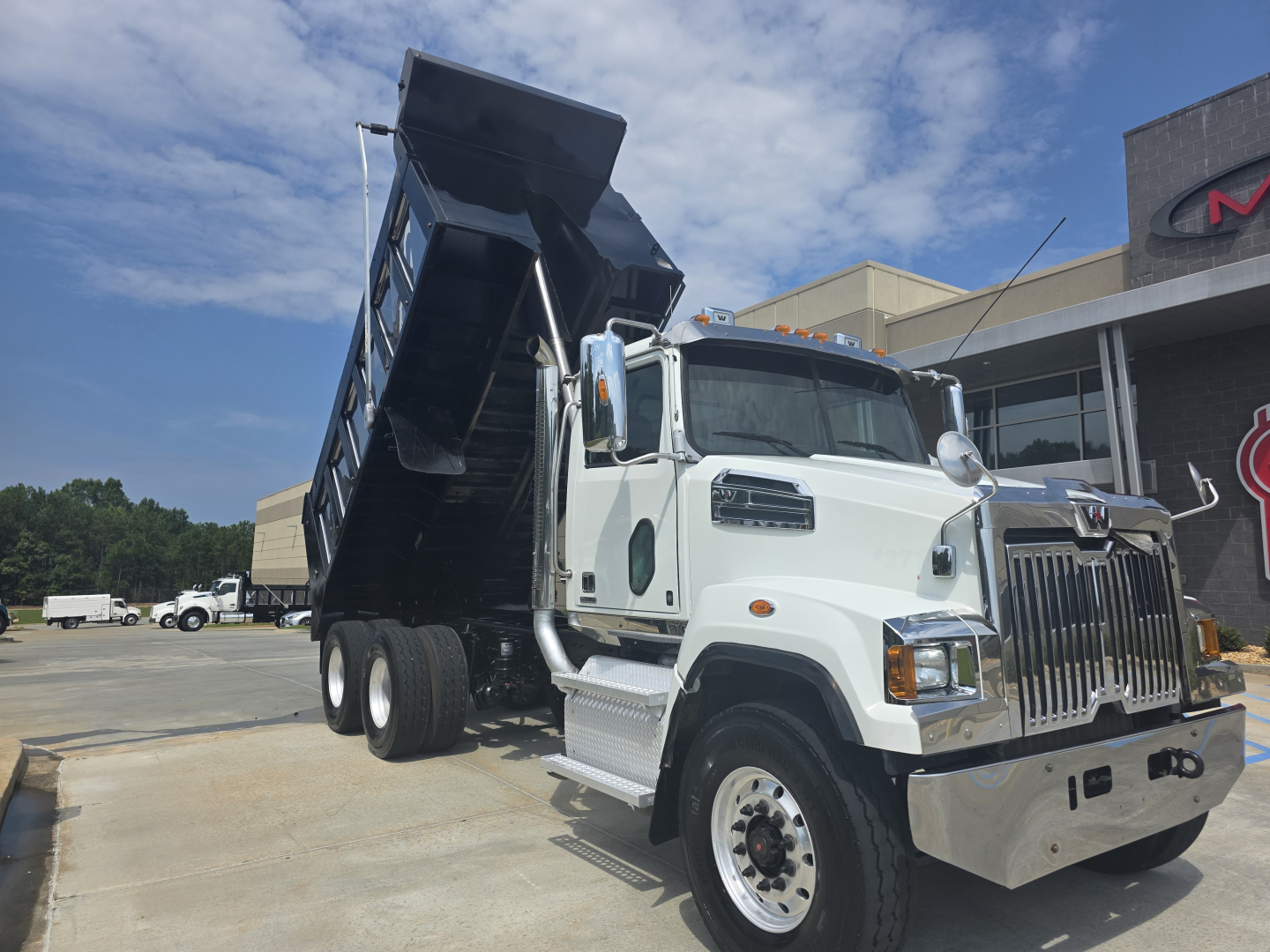White Western Star 4700SF dump truck with dump bed raised, front grille chrome, side mirrors, and sticker text visible on cab.