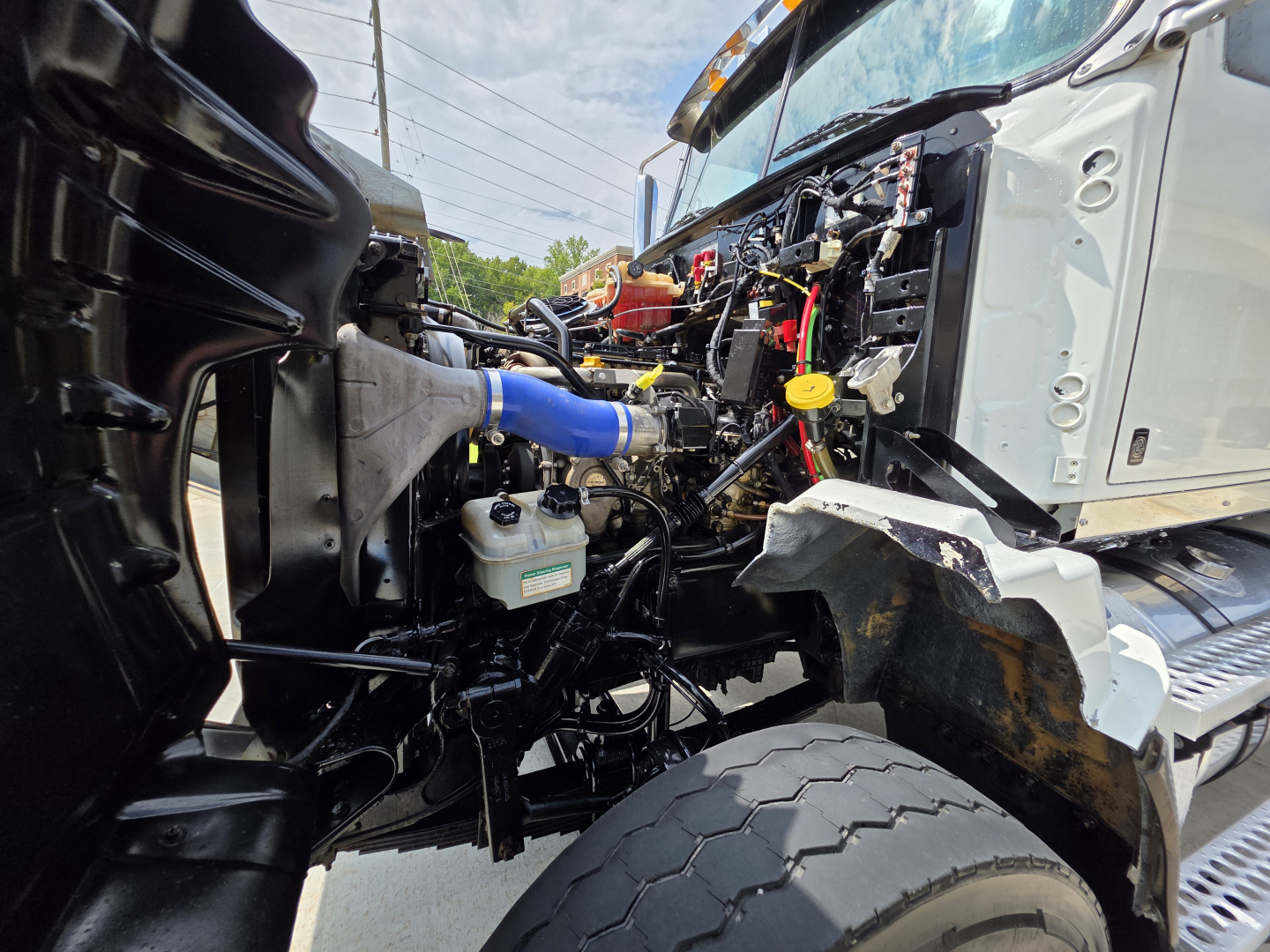 Western Star 4700SF engine bay with exposed components including blue hose, yellow dipstick, white reservoir, and various wires.