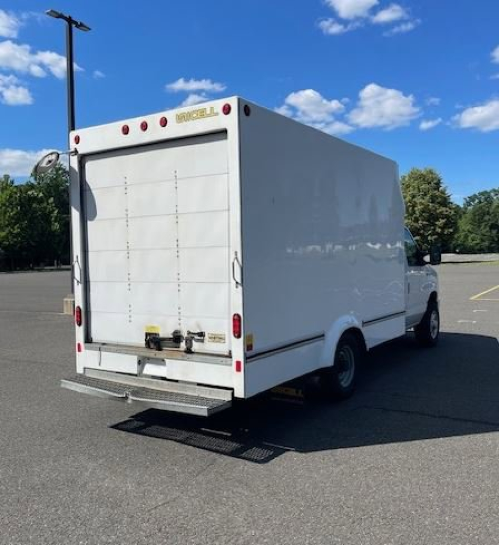 Box truck rear view showing E-Series cutaway cargo box with ramp and rear doors; white exterior, blue sky, tail lights, and bumper undercarriage.