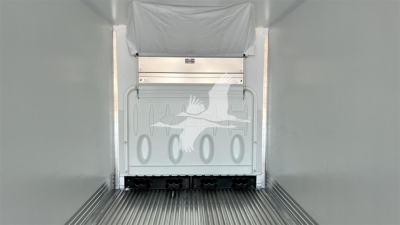 Trailer interior showing cargo area with ribbed floor and a rear door with cutout pattern of airplane silhouettes and circular openings.