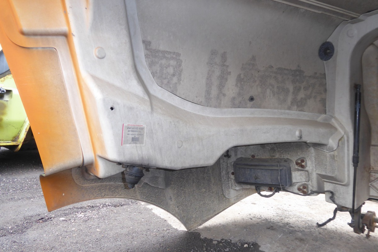 Volvo VNM hood area showing inner metal panel and label near lower edge. View of underside with hinge and wiring harness.
